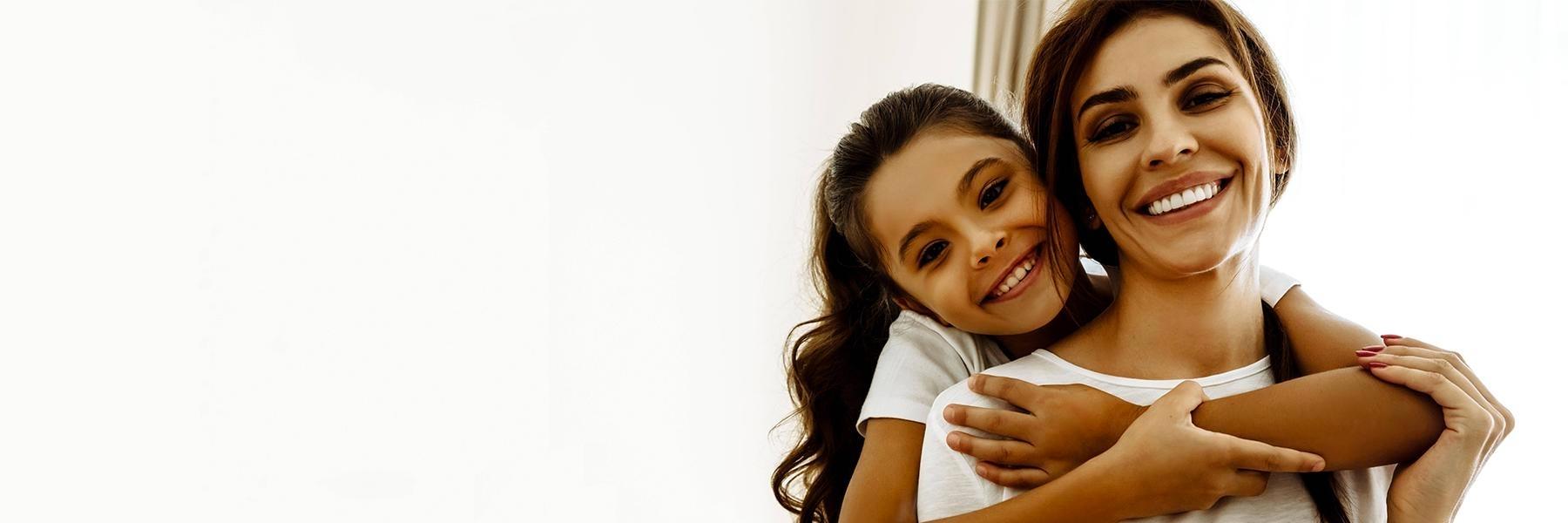 young girl hugging her mom's shoulders from behind