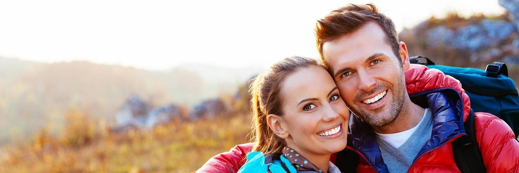 Man and woman smiling with bright smiles while out on a hike